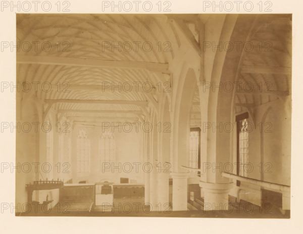 Interior of the large church in Vollenhove, photograph, annotation: 'Interior of the large church in Vollenhove (O.IJ.) Aug 1898', annotation: 'Vollenhove', Vollenhove, 1898, photographer, Attributed to, paper, pasteboard, albumen print, height 167 mm x width 230 mm, interior of church, A sepia-toned interior view showing a vaulted wooden ceiling with exposed curved beams and horizontal rafters, tall arched openings supported by round columns with capitals, narrow tall windows with patterned panes set between the arches, wooden gallery rails and pews visible below, a hanging ornate circular chandelier on one side, and various wooden panels and furnishings along the back wall.
