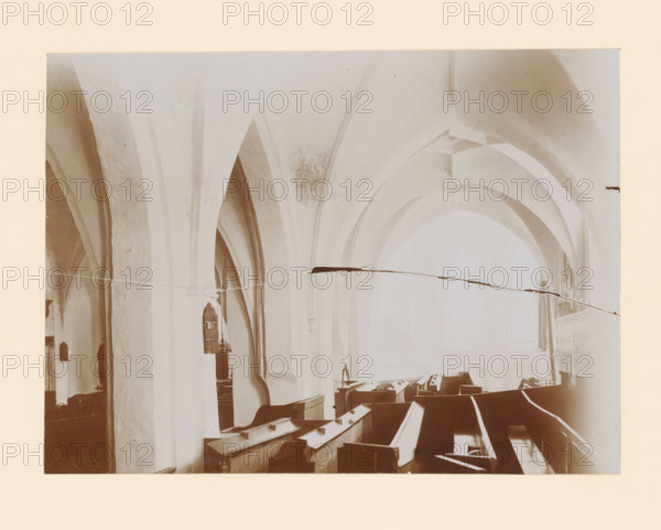 Interior of the St. Nicholas Church in Wijhe, photograph, annotation: 'Dutch Reformed Church in Wijhe Aug 1911', annotation: 'Wijhe', St. Nicholas Church (Wijhe), 1911, photographer, Wijhe, Attributed to, paper, pasteboard, daylight collodion silver print, height 160 mm x width 220 mm, interior of church, A high interior view of a vaulted space showing tall, pale arched columns and ribbed ceilings, with rows of wooden pews filling the lower area, a lectern or pulpit visible along one side, soft light coming through large arched windows, and subtle discoloration and cracks on the plaster surfaces.