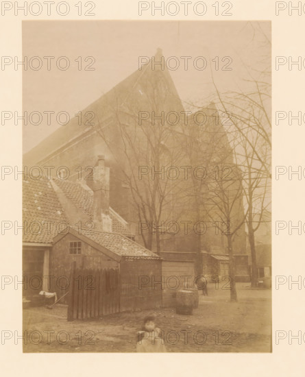 View of the Broerenkerk in Zwolle, photograph, annotation: 'Zwolle', annotation: 'Boerenkerk te Zwolle (O.IJ.)', Zwolle, 1899, photographer, Attributed to, paper, pasteboard, albumen print, albumendruk, height 228 mm x width 170 mm, church (exterior), Broerenkerk, A faded sepia photograph showing rooftops and a large steep gabled building partially obscured by leafless trees, with tiled roofs and a chimney in the foreground, a small wooden shed with a single window and a fenced gate, a dirt yard with scattered objects including a barrel and a low stone, a person standing near the trees in the middle distance, and a blurred child in the foreground.