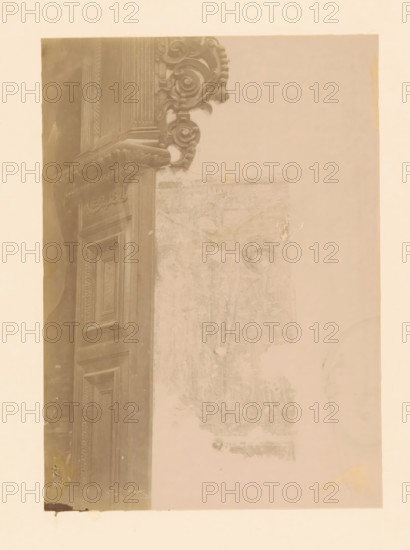 Mural in the St. Michael's Church in Zwolle, photograph, annotation: 'Zwolle: found mural in the St. Michael's Church', annotation: 'Zwolle', Zwolle, 1890 - 1910, photographer, Attributed to, paper, pasteboard, albumen print, height 235 mm x width 168 mm, interior of church, painting (including book-illumination, miniature-painting), A faded photographic print shows a vertical section of an ornate wooden doorway with carved panels and decorative molding on the left side, adjacent to a worn wall surface with faint, partially erased painted imagery and a small patch of peeled paper toward the center right; the photograph has a pale, sepia tone overall, with a light border around it and areas of discoloration and minor tears near the edges.