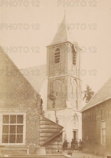 Tower of the Village Church of Nootdorp, photograph, annotation: 'Tower of the church of the Dutch Reformed congregation in Nootdorp, June 1891', annotation: 'Dutch Reformed Church, Tower, June 1891, Nootdorp', Nootdorp, 1891, photographer, Attributed to, paper, pasteboard, albumen print, height 239 mm x width 169 mm, parts of church exterior and annexes: tower, street (city(-scape) with figures, staffage), A tall brick church tower with a pointed roof and a circular clock face on one side rises between adjoining brick buildings, showing arched openings and louvers on the upper section and decorative brickwork on the lower section; in front of the tower a small courtyard area is visible with a wooden stepped structure and a barrel, a window with panes to the left, and a group of people standing near a gate by an arched doorway beneath the tower, while tiled roofs and a few small trees frame the scene.