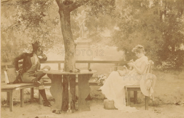 Photo reproduction of the painting In Love by Marcus Stone, In Love, cabinet photograph, reproduction, collector's mark: 'Vosmaer', stamp: 'WF Nollée, Papier- & Kunsthandel, Painting & Drawing Needs, Wilhelminagallerij, The Hague', inscription: 'Photographic Gesellschaft, Berlin, Gegründet 1862.', after painting by Marcus Stone, publisher: Photographische Gesellschaft Berlin, 1870 - 1890, Marcus Stone, Photographische Gesellschaft Berlin, photographer, after painting by, publisher, pasteboard, paper, albumen print, albumendruk, height 109 mm x width 169 mm, couple of lovers, A sepia-toned outdoor scene showing a wooden round table with a tree trunk rising through its center, a few round objects on the table surface, and a man seated on a bench to the left wearing a dark jacket, light trousers, high boots, and a pointed hat while leaning on one hand and resting the other on his hip. To the right a woman in a light flowing dress sits on a chair with a wide-brimmed hat hanging from the ch...