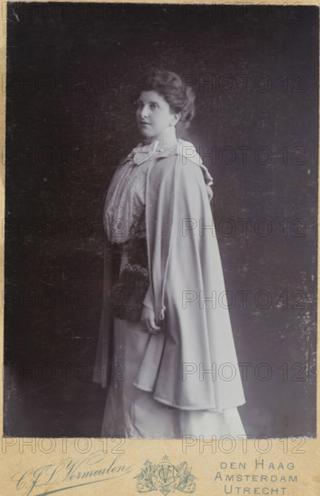 Portrait of an unknown standing woman, photograph, cabinet photograph, Possibly a portrait of a writer., :, inscription: 'CJL Vermeulen, THE HAGUE, AMSTERDAM, UTRECHT', Toussaintkade 11., Intercommunal Telephone: 774., UTRECHT, Nieuwe gracht 50., Telephone No 750.', photographer: Cornelis Johannes Lodewicus Vermeulen, The Hague (possibly), Utrecht (possibly), 1871 - 1936, Cornelis Johannes Lodewicus Vermeulen, paper, pasteboard, daylight collodion silver print, height 141 mm x width 102mm, height 165mm x width 108 mm, historical persons not known by name, standing figure (canon, proportions) - AA - female human figure, A black and white portrait of a woman shown in profile, facing left, wearing a high-collared blouse with a large bow at the neckline and a long flowing cape draped over her shoulders; her hair is styled up and appears softly waved, her expression is neutral, and one hand hangs down at her side holding the edge of the cape.