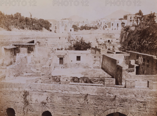 Panorama di Ercolano, View of ruins at Herculaneum, Italy, photograph, number: 'No. 1291', collector's mark: 'VOSMAER', photographer: Giorgio Sommer, Herculaneum, 1857 - 1875, Giorgio Sommer, photographer, pasteboard, paper, albumen print, height 315 mm x width 421 mm, urban housing, city-view in general, 'veduta', ruin of a building, architecture, destroyed, ruined place or city (, warfare), A sepia-toned scene of layered stone ruins and buildings with flat roofs and rectangular openings, showing exposed brickwork, archways, and remnants of walls at various heights; trees and dense foliage appear on the right and along the upper terrace, with more clustered buildings and terraces in the background; the foreground features textured masonry with patterned brick sections and dark arched openings at the bottom, while scattered stairways, small barred windows, and a few roofed shelter structures are visible among the crumbling platforms and courtyards.