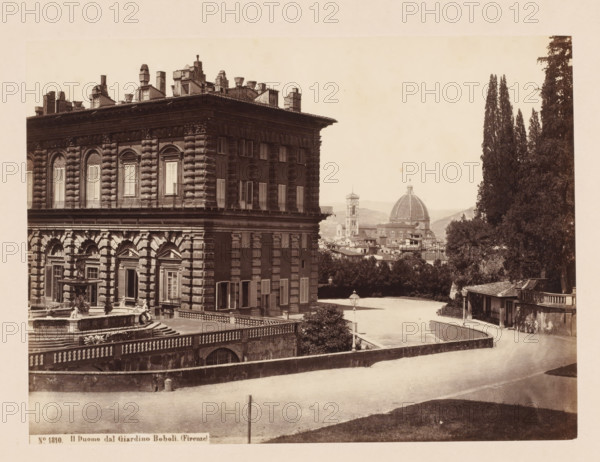 Il Duomo dal Giardino Boboli. (Firenze), View of the Pitti Palace, the Boboli Gardens and the Duomo of Florence, Italy, photograph, address: 'SOMMER E BEHLES, NAPOLI Monte di Dio 4, DEPOT A FLORENCE, VIA MAGGIO 15', number: 'No. 1810.', photographer: Sommer & Behles, Florence, 1867 - 1874, Tuscany, pasteboard, paper, albumen print, height 307 mm x width 375 mm, park, church (exterior), tower (of house or building), hôtel, ie small palace in city, Florence Cathedral, Palazzo Pitti, Giardino di Boboli, A sepia-toned scene showing the corner of a large ornate stone building with rusticated masonry, tall shuttered windows, decorative cornices, and a balustraded terrace with a sculpted fountain in front; a broad paved area and curved driveway run alongside the building, bordered by low stone walls and a lamppost, with a cluster of tall cypress trees and other foliage rising on the right; in the middle distance a domed cathedral and a bell tower rise above a cityscape of tiled roofs and dist...
