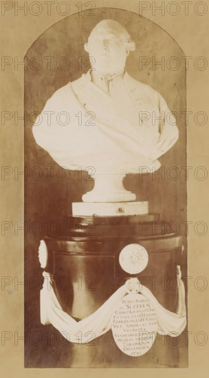 Bust of Pierre André de Suffren de Saint-Tropez, photograph, after sculpture by Jean Antoine Houdon, 1890 - 1920, Jean Antoine Houdon, photographer, after sculpture by, paper, pasteboard, baryta paper, gelatin silver print, developing gelatin silver print, height 283 mm x width 158 mm, Person, Pierre André de Suffren de Saint-Tropez, piece of sculpture, reproduction of a piece of sculpture, historical persons, A marble bust of a man with a high collar and draped garment sits on a rounded pedestal within an arched niche, the bust showing facial features, hair styled back, and a sash across the chest; the pedestal has a dark cylindrical base with decorative round medallions and a draped cloth element hanging in front, and the overall scene is in warm sepia tones with visible surface texture on the niche walls.