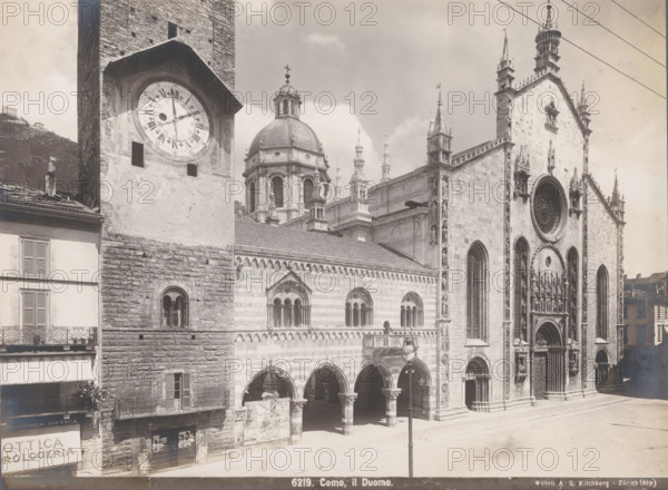 Como, il Duomo, View of the Como Cathedral, photograph, collector's mark: 'VOSMAER', number: '6219.', photographer: Gebrüder Wehrli, 1897 - 1924, Gebrüder Wehrli, photographer, Lombardy, paper, baryta paper, gelatin silver print, developing gelatin silver print, height 162 mm x width 218 mm, church (exterior), Cathedral of Como, A large stone cathedral facade with ornate arches, sculpted figures, a circular rose window, and pointed spires stands beside a tall clock tower showing a round clock face; the stonework varies between rough blocks and smoother dressed masonry, and there are arched walkways and columns at street level. A domed structure with windows and decorative balustrades rises behind the main building. To the left, a multi-story building with shuttered windows and wrought-iron balconies is visible. Street lamps and overhead wires cross the scene, and posters are attached to a lower wall near the arches. The sky above is partly cloudy.