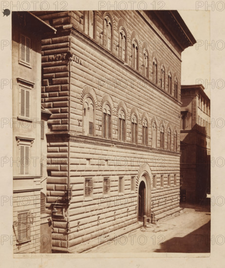 Façade of Palazzo Strozzi in Florence, Palazzo Strozzi Firenze, photograph, number: 'No. 1823.', Florence, c. 1875 - c. 1900, photographer, Tuscany, paper, pasteboard, albumen print, height 247 mm x width 197 mm, palace, façade (of house or building), A sepia-toned photograph showing the facade of a large stone building with rusticated masonry and rows of arched windows with decorative surrounds, a tall arched doorway set into the wall, smaller barred windows near the ground, and metal rings attached to the lower stone courses; adjacent on the left is a narrower building with shuttered windows and a small awning, while a shadowed narrow street runs alongside the right side and another building with shuttered windows is visible in the background.