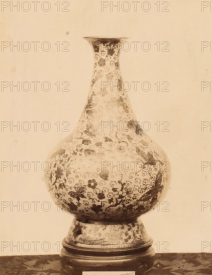 Vase decorated with floral motif and butterflies, photograph, number: '4.', c. 1875 - c. 1900, photographer, paper, pasteboard, albumen print, albumendruk, height 257 mm x width 199 mm, flowers, ornament, insects: butterfly, container of ceramics: jar, jug, pot, vase, ornamenting, decorating, applied arts, A tall, rounded vase with a narrow neck and flared rim sits on a short pedestal base, both covered in a dense floral pattern of small blossoms and curling vine motifs; the surface shows areas of darker staining and wear, and the image has a warm, sepia tone with a plain, lightly mottled background.