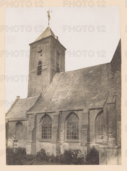 South side of the Old Church in Naaldwijk, photograph, annotation: 'Jz. Sweerts, ca. 1620', annotation: 'South side Dutch Reformed Church, May 1910, Naaldwijk', Naaldwijk, 1910, photographer, Attributed to, paper, pasteboard, gelatin silver print, height 218 mm x width 158 mm, church (exterior), A sepia-toned photograph showing the exterior of a brick building with a steep tiled roof and a square tower rising above it. The tower has a pitched roof topped by a metal weather vane, circular clock faces set into the brick walls, and arched openings with visible louvered slats. The building facade below features tall arched windows with multiple panes, brick buttresses, and sections of stone cladding at the base. Vegetation grows along the ground in front of the building. The sky above is pale and uniform.