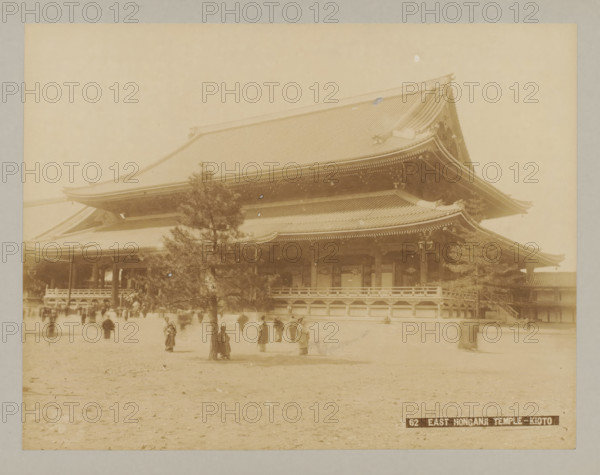 62 East Honganji Temple-Kioto, East side of Nishi Honganji Temple, Kyoto, photograph, number: '8.', c. 1895 - c. 1915, photographer, Kinki, paper, pasteboard, albumen print, albumendruk, height 209 mm x width 272 mm, height 243 mm x width 329 mm, A sepia-toned photograph showing a large traditional wooden temple building with a multi-tiered sweeping roof and ornate eaves, a raised veranda with railings, columns, and carved details, a tree in the foreground partially obscuring the temple, and a flat open ground in front where several people in period clothing stand or walk.