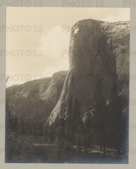 Yosemite Valley, photograph, At the bottom it says: 10007., annotation: '1. Yosemete-Valley, California', California, c. 1895 - c. 1915, photographer, North America, paper, pasteboard, gelatin silver print, developing gelatin silver print, height 239 mm x width 189 mm, height 329 mm x width 243 mm, A tall, steep rock face rises prominently on the right side of the image, showing smooth, vertical surfaces and textured cliff edges, with a ridge of trees along its top. A densely wooded valley sits below and to the left of the rock face, with dark tree canopies and scattered lighter patches of exposed rock. A river winds through the lower part of the scene, bordered by trees and shaded areas. Soft clouds occupy the upper left sky, creating a pale contrast against the darker cliffs and forest. The image has a uniform border around it.