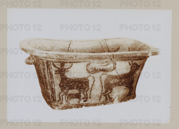Red earthenware bathtub from the Palace of Knossos, photograph, Bathtub decorated with three animals., annotation: '56. Crete. Palace at Knossos. Red earthenware bathtub.', unknown, c. 1895 - c. 1915, photographer, pasteboard, paper, daylight gelatin silver print, height 162 mm x width 233 mm, height 239 mm x width 328 mm, Crete, Knossos, A photograph of the upper portion of a weathered ceramic vessel with a wide rim and rounded interior, shown against a plain light background with a narrow border; the vessel surface is light with darker painted figures, including animal motifs that resemble horned and hornless quadrupeds in profile, stylized decorative bands and vertical panels, visible cracks and areas of wear and flaking on the rim and body, and small handles or projections at the rim sides.