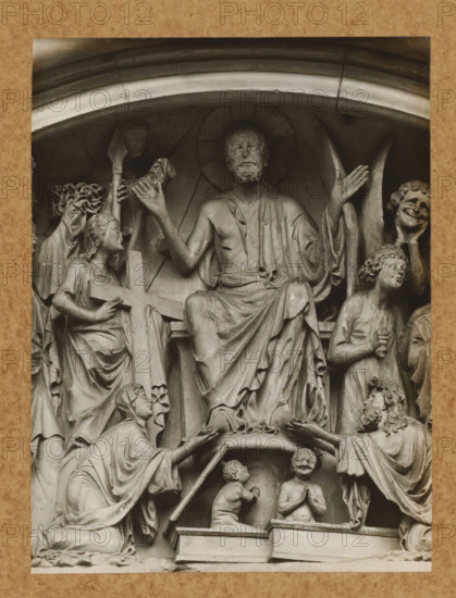 Detail of the tympanum of the Fürstenportal in Bamberg Cathedral, Fürstentor, Tymphanon, Christ from the front, album page, photograph, This photo is part of an album., number: '113', Bamberg, 1900 - c. 1920, photographer, Bavaria, paper, baryta paper, gelatin silver print, height 217 mm x width 163 mm, church (exterior), Bamberg Cathedral, A carved stone relief showing a seated bearded man with a halo and draped robes, his arms raised and palms open, surrounded by multiple figures in flowing garments; to his left a kneeling woman holds a large cross while another figure reaches upward with a spear-like object, to his right a standing figure with curly hair looks upward and a smiling masked face is held by a hand; below the central figure two small childlike figures kneel on a platform, one with hands together and the other turned toward the central figure, while a robed figure on the lower left kneels and extends an object toward the central scene.