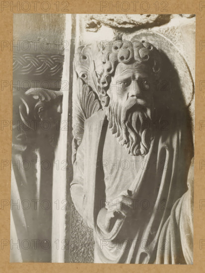 Georgenchorschranken, Prophetenrelief (n.SS) 1.Prophet v.li. (Kopf vv), Detail of the rood screen in the East Choir of Bamberg Cathedral, album page, photograph, This photo is part of an album., number: '118.', Bamberg, 1900 - c. 1920, photographer, Bavaria, paper, baryta paper, gelatin silver print, developed gelatin silver print, height 219 mm x width 160 mm, interior of church, Bamberg Cathedral, A close-up photograph of a carved stone figure showing a bearded man with curled hair and a flowing beard, his face turned slightly toward the viewer with a solemn expression, wearing draped robes and holding a staff or rod; ornate carved foliage and decorative patterns appear behind and beside him, and a second carved face is partially visible in shadow to the left.