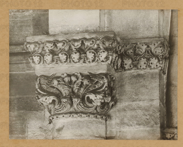 East church, with Triumphal arch chapter, Capital of Bamberg Cathedral, album page, photograph, This photo is part of an album., number: '13.', Bamberg, 1900 - c. 1920, photographer, Bavaria, paper, baryta paper, gelatin silver print, height 165 mm x width 214 mm, church (exterior), Bamberg Cathedral, A close-up view of a carved stone capital and surrounding masonry showing ornate acanthus leaf and scroll motifs in a weathered light-toned stone, with a horizontal band of rounded carved elements above and textured blocks of stone forming the wall and column surfaces, all framed by a narrow darker border.