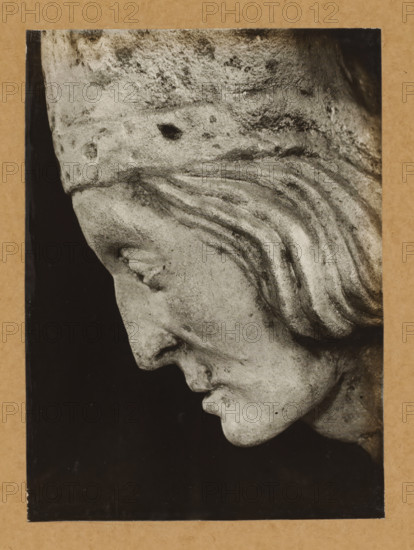 Sculpture of Friedrich I von Hohenlohe in the cathedral of Bamberg, Kreuzgang, Grabmal Friedrich v.Hohenlohe, Profil v. right, album page, photograph, This photo is part of an album., number: '155', Bamberg, 1900 - c. 1920, photographer, Bavaria, paper, baryta paper, gelatin silver print, developing gelatin silver print, height 225 mm x width 164 mm, Person, Friedrich I. von Hohenlohe, interior of church, Bamberg Cathedral, A close-up black-and-white photograph of a stone sculpture showing a downward-facing profile of a human head with carved hair in wavy strands, a pronounced brow and nose, closed eye, and a slightly open mouth, mounted on a rectangular frame with a dark background and a textured border.
