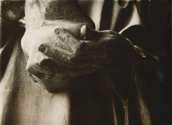 Detail of the Adamspforte in the cathedral of Bamberg, Adamspforte, Stephanus (1.Hand), album page, photograph, This photo is part of an album., inscription: 'Kunsthist. Seminar, Marburg (Lahn), Photogr. Abteilung, Vervielfältigung, untersagt.', Bamberg, 1900 - c. 1920, photographer, Bavaria, paper, baryta paper, gelatin silver print, developing gelatin silver print, height 180 mm x width 238 mm, Person, Stephen (martyr), church (exterior), Bamberg Cathedral, A close-up sepia-toned image of a weathered stone hand resting palm-up, showing rough texture and worn edges, with draped fabric folding around the wrist and background, shadows emphasizing the contours and surface variations.