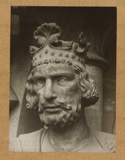 Adamspforte (Kaiser Heinrich) (Head from front), Detail of the Adamspforte in Bamberg Cathedral, album page, photograph, This photo is part of an album., number: '45.', Bamberg, 1900 - c. 1920, photographer, Bavaria, paper, baryta paper, gelatin silver print, gelatin silver developing print, height 224 mm x width 163 mm, Person, Saint Henry II (Holy Roman Emperor), church (exterior), Bamberg Cathedral, A close-up photograph of a stone sculpture showing the head and upper torso of a bearded man wearing a detailed crown with decorative leaf-like and curled elements, visible weathering and surface texture on the stone, wavy hair framing the face, carved eyes and a solemn expression, a portion of draped clothing across the shoulders, and a dark background with a cylindrical column partially visible behind the head.