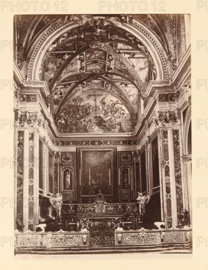 Interior of Chiesa di San Martino, Napoli Chiostro di S. Martino, album page, photograph, This photo is part of an album., workshop stamp: 'Giorgio Sommer, Largo Vittoria, Napoli', number: '8131', photographer: Giorgio Sommer, Naples, 1874 - in or before 1879, paper, albumen print, height 251 mm x width 182 mm, interior of church, A sepia-toned interior photograph showing an ornate chapel with a highly decorated vaulted ceiling featuring painted scenes and intricate arch moldings, flanked by elaborately carved pilasters and panels; a central altarpiece area with framed paintings and sculpted niches containing statues sits above a richly carved altar front with decorative reliefs and ornamental balustrades, and sculpted angelic figures positioned near the altar; patterns of marble, gilded ornamentation, and detailed architectural cornices run along the walls, while the lower foreground shows an ornamental railing with repeating carved motifs.