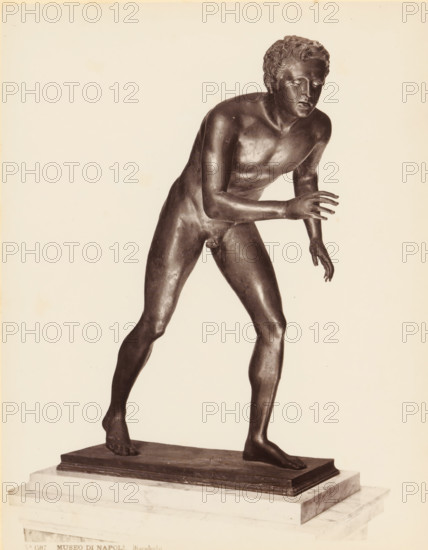 Bronze sculpture of an athlete, Museo di Napoli Discobolo, album page, photograph, This photo is part of an album., number: '1505', workshop stamp: 'Giorgio Sommer, Largo Vittoria, Napoli', photographer: Giorgio Sommer, Naples, 1874 - in or before 1879, paper, albumen print, height 251 mm x width 199 mm, sculpture (bronze, arts), athletics, gymnastics (sportsman, player, etc.), A dark-toned bronze statue of a nude young male figure is shown standing on a rectangular base placed on a marble plinth; the figure leans forward with one leg stepped ahead and the other trailing, one arm extended forward with fingers splayed and the other arm lowered and slightly bent, the head turned slightly to the side with curly hair and a focused facial expression, the surface of the bronze shows subtle highlights and patina, and the background is a plain light color.