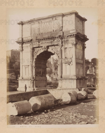 View of the Arch of Titus in the Roman Forum in Rome, album page, photograph, This photo is part of an album., inscription: '22 ARCO DI TITO', Rome, 1870 - c. 1895, photographer, paper, pasteboard, albumen print, height 258 mm x width 199 mm, triumphal arch, Arch of Titus, A large stone archway with decorative carvings and fluted columns dominates the scene, showing weathered surfaces and worn ornamentation, while a person stands near its base providing scale. Broken cylindrical stone drums lie scattered in the foreground on uneven ground. Behind and around the arch are ruined masonry and fragments of structures, with a building partially visible in the midground to the left and trees in the background. The image has a sepia tone and shows the monument mounted on a raised platform with steps and ledges.