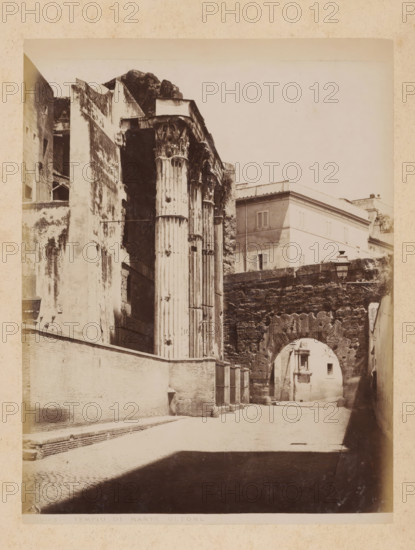 View of the Temple of Mars Ultor at the Forum of Augustus in Rome, album page, photograph, This photo is part of an album., inscription: '503 TEMPLO DU MARTE ULTORE', Rome, 1870 - c. 1895, photographer, paper, pasteboard, albumen print, height 260 mm x width 199 mm, ruin of a building, architecture, (story of) Mars (Ares), temple, shrine, Roman religion, Forum of Augustus, Temple of Mars Ultor, A sepia photograph shows a narrow street flanked by high walls and ancient stone structures, with tall, fluted columns topped by ornate capitals visible on the left and an arched stone passageway spanning the street further back on the right; buildings with shuttered windows sit above the arch, and a street lamp is mounted on the wall near the arch; the ground is paved and a deep shadow falls across the foreground of the scene.