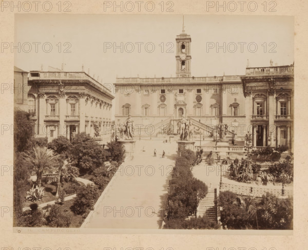 View of the Capitol in Rome, album page, photograph, This photo is part of an album., inscription: '60 IL CAMPIDOGLIO', Rome, 1870 - c. 1895, photographer, paper, pasteboard, albumen print, height 200 mm x width 256 mm, prospect of city, town panorama, silhouette of city, square, circus, palace, Capitol, A wide sepia photograph of a large classical building with a tall clock tower rising from its center and flanked by symmetrical wings, ornate façades with columns and arched windows, and a broad central staircase leading down to a paved open terrace; stone statues and sculpted figures stand atop pedestals along the terrace and at the top of the stairs, with a pair of equestrian figures visible; trees, shrubs, and landscaped gardens border a long central walkway that runs from the foreground toward the staircase, with a few small human figures walking on the path; ornamental railings, lamp posts, and stone balustrades appear along the stairs and terraces, and the scene is framed by addi...
