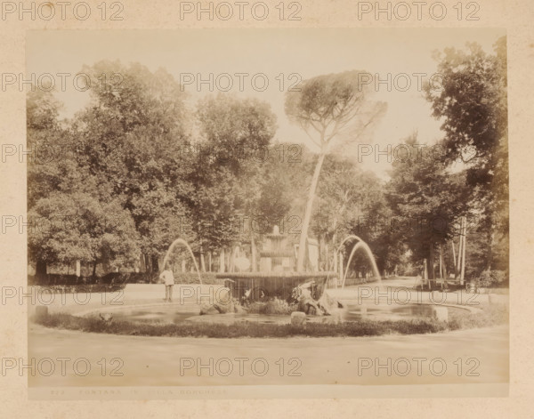 View of the Fontana dei Cavalli Marini in the Villa Borghese in Rome, album page, photograph, This photo is part of an album., inscription: '272 FONTANA IN VILLA BORGHESE', Rome, 1870 - c. 1895, photographer, paper, pasteboard, albumen print, albumendruk, height 201 mm x width 262 mm, park, ornamental fountain, Villa Borghese, A faded monochrome photograph of a tree-lined park area with a central ornamental fountain, water arcing from jets into a circular basin, sculptural elements at the fountain base, a standing figure near the fountain wearing a light-colored outfit, dense clusters of tall trees forming a canopy behind the fountain, a paved walkway curving around the fountain, and a distant row of trees and open space receding into the background.