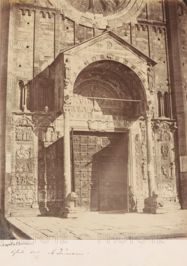 Portal of the Basilica di San Zeno (also: San Zeno Maggiore), Verona, Italy, photograph, Italy., date: '1860's', stamp: 'Fotografia E. Bressanini', caption: 'ogliti di St. Zinone ?', number: '1183.', photographer: Emilio Bressanini, c. 1865 - c. 1880, Emilio Bressanini, photographer, pasteboard, paper, albumen print, height 276 mm x width 218 mm, height 411 mm x width 301 mm, S. Zeno, A sepia-toned photograph of an ornate stone entrance with a large arched portal set into a brick façade, flanked by carved columns and sculpted relief panels; the arch contains decorative carvings and a recessed semicircular tympanum with figures, and a wide painted shadow crosses the doorway and surrounding stonework; tall carved doors with square panels occupy the central opening, and sculpted lion figures sit at the base of the columns on either side of the steps; a person stands near the right column partially in shadow; the ground in front is paved with large stone slabs and the upper wall shows rows...