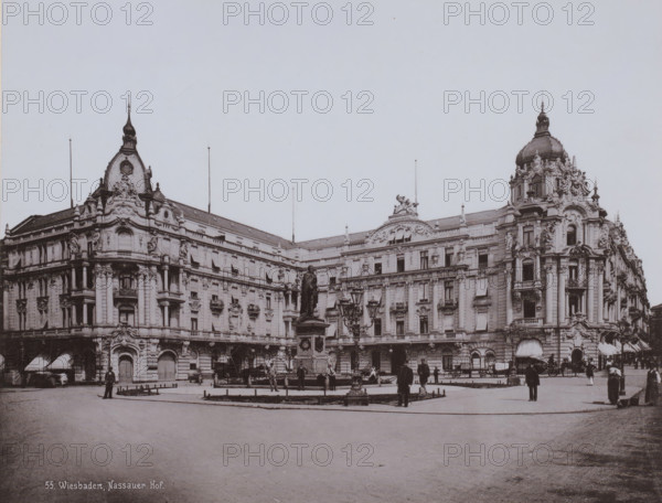 Hotel ? Nassauer Hof, Wiesbaden, Germany, photograph, Germany., inscription: '55. Wiesbaden, Nassauer Hof.', c. 1885 - c. 1900, photographer, pasteboard, paper, collotype, photoprint, height 213 mm, width 275 mm x width 330 mm, height 510 mm, Hessen, A wide facade of an ornate stone building with decorative sculpted details and domed towers stretches across the scene, with multiple windows, balconies, and columns visible; a central plaza in front features a raised pedestal topped by a statue of a standing figure and surrounded by lamp posts and a low fenced planter, while several people in period clothing and a few horse-drawn carriages are scattered around the plaza and near the building entrances.