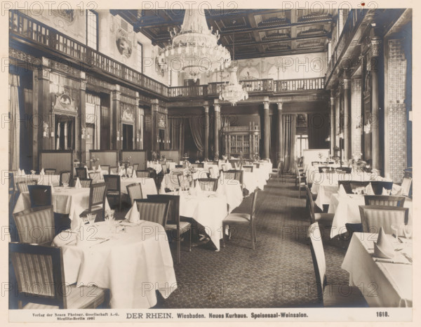 Speisesaal, Weinsalon, Neues Kurhaus, Wiesbaden, Germany, photograph, Germany., caption: 'DER RHEIN. Wiesbaden. Neues Kurhaus. Speisesaal-Weinsalon.', name: 'Neue Photographische Gesellschaft AG, Steglitz-Berlin 1907', number: '1618.', photographer: Neue Photographische Gesellschaft, Berlin, 1907, pasteboard, paper, albumen print, albumendruk, height 189 mm, width 245 mm x width 328 mm, height 510 mm, Hesse, A wide dining room with cloth-covered round and rectangular tables arranged in rows, each table set with folded napkins, glassware, and small floral centerpieces, surrounded by wooden chairs with upholstered seats and striped backs; tall decorative columns and wood-paneled walls rise to a balcony level with balustrades, ornate carved moldings, framed medallion reliefs, and draped curtains; two large crystal chandeliers hang from a coffered ceiling, and patterned carpeting covers the floor.