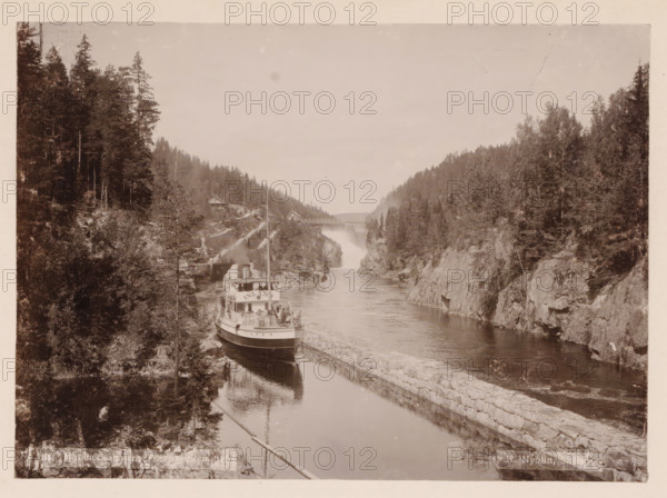 Vrangfos, Telemarken, photograph, Frontal view of a boat passing through a lock, with the river alongside. The Telemark Canal (Telemarkskanalen) in Norway consists of two canals, of which the Norsjø-Skien Canal with locks in Skien and Løveid, built between 1854 and 1861, is the oldest of the two canals. The other canal we see in the photo is the Bandak-Norsjø Canal, opened in 1892 =terminus post quem., caption: 'No. 5 Vrangfos, Telemarken sic., R. Nyblin, Skien., Eneberettiget 1896.', photographer: Ragnvald Nyblin, Skien, in or after 1896 - c. 1915, Telemark, paper, pasteboard, daylight collodion silver print, daylight collodion silver print on photo paper on cardboard, height 157 mm, width 218 mm x width 311 mm, height 380 mm, A sepia-toned scene of a narrow river flanked by steep rocky banks covered in dense trees, with a passenger steamship moored along a stone-lined channel near the left bank, its upper deck populated by people and railings and a tall smokestack rising above; a win...