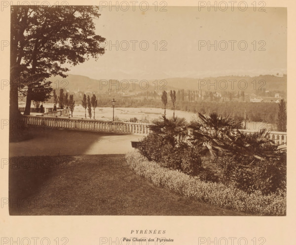 Pyrénées, Peau Chaine des Pyrénées', Pyrenees, France, photograph, View from a park over the landscape, with houses and mountains in the background., date: '8, 10 October 1884.', inscription: 'Pyrénées, inscription: 'Papeterie & Librairie, LAFON, 3. Rue Henry IV. 3, PAU, EAUX-BONNES, Etablissement Thermal', vendor: Lafon, Pau, 1884-10-08 - 1884-10-10, photographer, pasteboard, paper, albumen print, albumendruk, height 192 mm, width 253 mm x width 385 mm, height 340 mm, A sepia-toned scene showing a riverside landscape viewed from a terrace with a balustrade, framed at left by large tree trunks and leafy branches and at right by palms and dense shrubs, with a paved area and manicured lawn in the foreground, a lamp post near the railing, slender trees along the riverbank, a wide river beyond them, rolling hills with scattered buildings and tree lines in the middle distance, and a pale sky above.