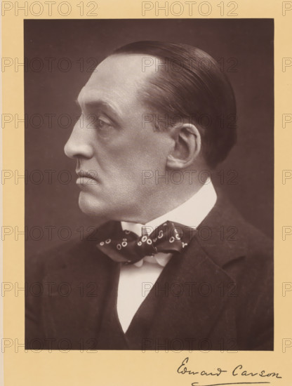Sir Edward Henry Carson, photograph, Portrait of a man and profile, caption: 'The Right Honorable Sir Edward Henry Carson, KC, LL.D.', caption: 'Russell & Sons, Photographers, Copyright., 17, Baker St., London W.', caption: 'Edward Carson', photographer: Russell & Sons, London, c. 1890 - c. 1910, pasteboard, paper, carbon print, height 225 mm, width 170 mm x width 263 mm, height 366 mm, A sepia-toned portrait of a man in profile facing left, showing a smooth, slicked-back hairstyle, a pronounced nose, a high forehead, and a clean-shaven face with visible skin texture; he is wearing a white shirt with a high collar, a patterned bow tie, and a dark suit jacket, and the photograph is mounted on a pale mat with part of a handwritten signature visible at the bottom edge.