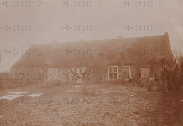 Aytta State (house of God or church) in Swichum, photograph, annotation: 'Aytta State House in Swichem, Ph ? Dec 1909, Friesland', Swichum, photographer: AJM Mulder (possibly), 1909, Attributed to, paper, pasteboard, daylight collodion silver print, height 150 mm x width 211 mm, church (exterior), A long, low brick building with a tiled roof and several chimneys stretches across the scene, fronted by leafless, gnarled trees and bare ground with patches of snow; there are multiple windows with visible panes, a few wooden doors, a ladder leaning against the wall, a barrel and scattered wooden boards near one end, and some low vegetation and rough earth in the foreground.