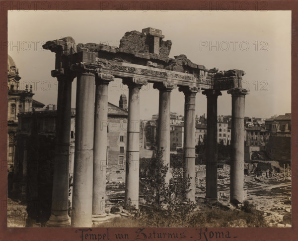 Temple of Saturn, Rome, Roman Forum, Italy, album page, photograph, Italy., inscription: 'Temple of Saturn - Roma', c. 1900 - c. 1940, photographer, pasteboard, paper, albumen print, height 185 mm x width 242 mm, height 207 mm x width 263 mm, A sepia-toned photograph of a row of tall stone columns with ornate capitals supporting a partially ruined entablature, with broken masonry and rubble atop the structure; behind and between the columns are glimpses of older buildings, rooftops, and a bell tower rising above surrounding structures; the foreground shows uneven ground, scattered stones, and vegetation at the base of the columns; to the left a portion of a domed building with decorative architectural details is visible, and to the right more urban buildings extend toward the horizon under a clear sky.