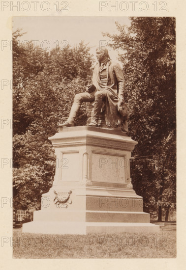 Statue of Robert Burns in Washington Park in Albany, photograph, page, Albany (New York), 1889, photographer, North America, paper, albumen print, height 144 mm x width 97 mm, monument, statue, A sepia-toned photograph of a seated statue atop a multi-tiered stone pedestal surrounded by trees, showing a robed male figure with one leg bent and the other extended, wearing a long coat and boots, holding a hat in one hand and resting the other on his knee, with detailed folds in the clothing and textured hair, the pedestal featuring recessed panels and decorative molding, grass at the base, and dense foliage filling the background.