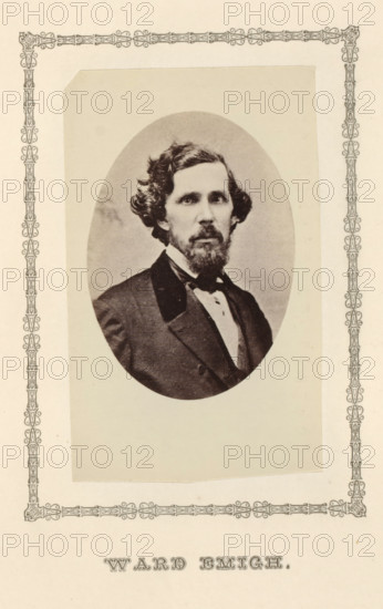 Ward Emigh, photograph, page, c. 1876 - in or before 1881, photographer, paper, albumen print, height 97 mm x width 60 mm, adult man, An oval-framed black-and-white portrait of a man with wavy hair and a full beard and mustache, wearing a dark suit jacket, a white shirt, and a bow tie, centered on a light rectangular mat with decorative patterned borders along the page edges.