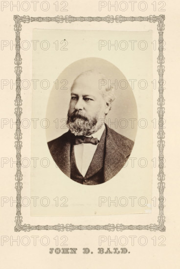 John D. Bald, photograph, page, c. 1876 - in or before 1881, photographer, paper, albumen print, height 95 mm x width 64 mm, adult man, An oval sepia portrait of a middle-aged man with a full beard and mustache, light-colored hair, and a serious expression, shown from the chest up wearing a dark suit jacket, waistcoat, white shirt, and a bow tie, centered on a pale rectangular mat with an ornate decorative border around the mat and some small spots and signs of age on the paper.
