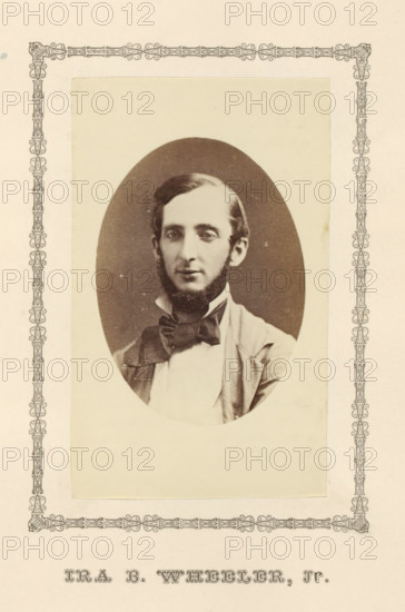 Ira B. Wheeler, Jr., photograph, page, c. 1876 - in or before 1881, photographer, paper, albumen print, height 100 mm x width 60 mm, adult man, A sepia-toned oval portrait of a young man with short dark hair and sideburns, wearing a light-colored shirt, a dark bow tied at his collar, and a jacket, set on a pale rectangular mount with a decorative border surrounding the mount and the page.