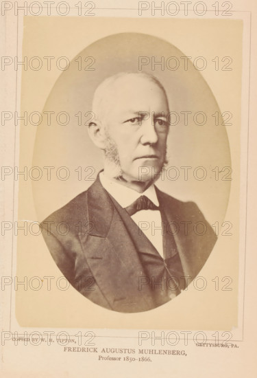 Fredrick Augustus Muhlenberg, photograph, page, photographer: William H. Tipton, Gettysburg, c. 1877 - in or before 1882, North America, Pennsylvania, paper, albumen print, height 146 mm x width 101 mm, Person, professor, A sepia-toned oval portrait of an older man shown from the chest up, wearing a dark suit jacket with a visible lapel, a vest, a white shirt with a high collar, and a dark bow tie; he has light-colored hair that is short and receding, prominent sideburns, a serious facial expression, and is looking slightly to the viewer's right, with a plain light background surrounding the oval and a pale rectangular border around the image.