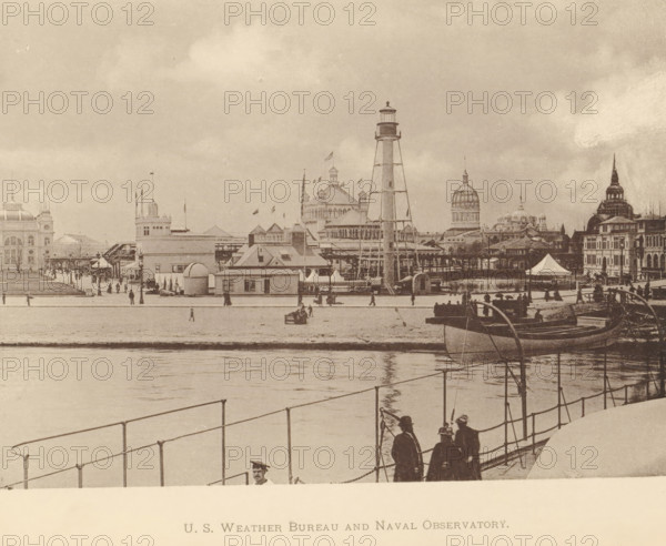 Coast Guard station and weather bureau at the World's Columbian Exposition in Chicago in 1893, US Weather Bureau and Naval Observatory, page, photomechanical print, Chicago, 1893, North America, Illinois, paper, collotype, photoprint, height 128 mm x width 177 mm, rowing-boat, canoe, world fair, world exhibition, World's Columbian Exposition, A waterfront scene in a sepia photograph shows a pier area with a railing in the foreground and calm water reflecting the shore. Several people stand near the railing, some wearing hats and coats, and a small group cluster together. Boats are moored along the shore, one prominent boat angled toward the viewer. On the opposite bank a row of buildings and pavilions rise, including a tall skeletal lighthouse tower, a domed building, and structures with turrets and flagpoles. Tents and smaller booths line the shore and a promenade runs along the water with scattered pedestrians. The sky above is cloudy and the overall image has an aged, grainy texture...
