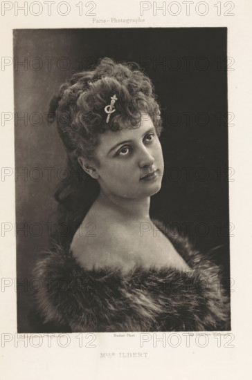 Mlle Ilbert, Portrait of Yvette Guilbert, page, photomechanical print, photographer: Félix Nadar, Paris, cliché maker: Dujardin, France, printer (person): Chardon-Wittmann, c. 1882 - in or before 1892, printer (person), paper, photoaquatint, height 159 mm x width 112 mm, Person, Yvette Guilbert, female singer, A sepia-toned portrait of a young woman shown from the shoulders up, her head tilted slightly and gaze directed upward and to the side, with tightly curled hair gathered and styled at the top and back, a decorative hairpin placed among the curls, clear eyes and delicate facial features, bare shoulders framed by a soft, plush fur wrap, and a plain dark backdrop inside a bordered rectangular frame on a light paper mount.