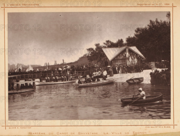 Baptism of the lifeboat La ville de Thonon, Baptême du canot de sauvetage 'La ville de Thonon', page, photomechanical print, photographer: E. Forestier, cliché maker: Adolphe Block, c. 1885 - in or before 1890, paper, Woodburytype, height 111 mm x width 168 mm, lifeboat, christening a ship, A sepia-toned scene shows a waterfront with several small rowboats on calm water, one in the foreground with a person wearing a hat rowing, and other boats nearer the shore with people seated or preparing to row. A wooden pier crowded with people extends along the shoreline, and a group of people stands on the sandy beach area near a pavilion-style wooden building decorated with hanging flags and trim. Trees rise behind the building, and additional crowds gather near the treeline and along the pier. Sails and masts are visible in the distance behind the pier, and the sky above is overcast.