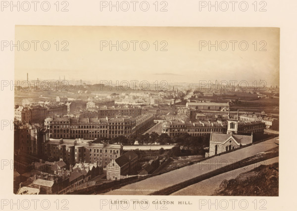 View of Leith, Leith, from Caltn Hill, photograph, page, photographer: Archibald Burns, Edinburgh, c. 1862 - c. 1867, paper, albumen print, height 154 mm x width 102 mm, Photo two pages after page 45., city-view in general, 'veduta', A wide sepia-toned panoramic view of a cityscape taken from an elevated vantage showing rows of multi-story stone buildings with pitched roofs and chimneys in the foreground, tree-lined streets and formal terraces of large rectangular buildings with repetitive windows and cornices, a church with a tower and arched windows near the right foreground, open grassy slopes and a sloping paved path in the lower right leading down toward the built area, densely packed residential blocks and narrow streets extending into a flatter middle ground with scattered industrial chimneys and low warehouses, expanses of lighter-toned open land and distant low hills on the horizon under a pale sky.