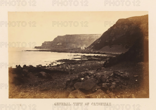 General view of Causeway, photograph, page, photographer: John Hudson, Giant's Causeway, c. 1862 - in or before 1867, John Hudson, photographer, Causeway Coast and Glens, paper, albumen print, height 109 mm x width 174 mm, landscapes with waters, waterscapes, seascapes (in the temperate zone), rock-formations, sea, A coastal landscape with a rocky shoreline in the foreground leading to a calm sea, a small white building near the water at the base of steep, dark cliffs, layered cliffs and a headland extending into the distance, scattered boulders and stones on the shore, reflections and shallow pools of water among the rocks, a pale sky above.
