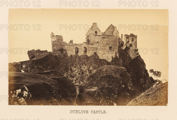 Dunluce Castle, View of Dunluce Castle, photograph, page, photographer: John Hudson, Giant's Causeway, c. 1862 - in or before 1867, John Hudson, photographer, Causeway Coast and Glens, paper, albumen print, height 108 mm x width 178 mm, castle, ruin of a dwelling, house, A sepia-toned photograph of a ruined stone fortress perched on a rocky promontory with crumbling walls and partially standing towers, showing rough stone textures, window openings, and jagged rooflines, surrounded by dark rocky cliffs and grassy slopes in the foreground and a pale, empty sky in the background.