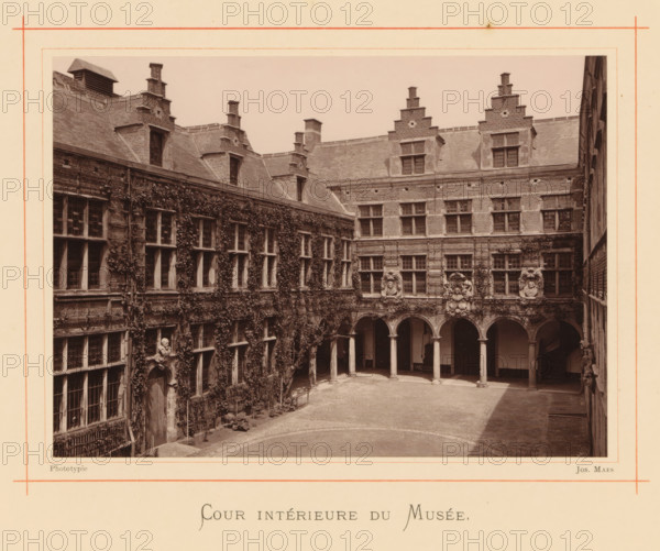 Courtyard of the house of Christoffel Plantijn, Cour intérieure du Musée, page, photomechanical print, maker: Joseph Maes, Antwerp, c. 1873 - in or before 1878, paper, Woodburytype, height 118 mm x width 164 mm, courtyard, A sepia photograph of a rectangular stone courtyard surrounded by multi-story brick and stone buildings with steep tiled roofs and stepped gables, featuring rows of rectangular windows with small panes and window frames, arched openings supported by columns along one side opening into a covered gallery, decorative stone medallions and sculpted reliefs above some arches, climbing vines covering large portions of one facade and winding around windows and doors, a cobbled or paved central ground area with a curved paving pattern near the foreground, and a framed border around the image.