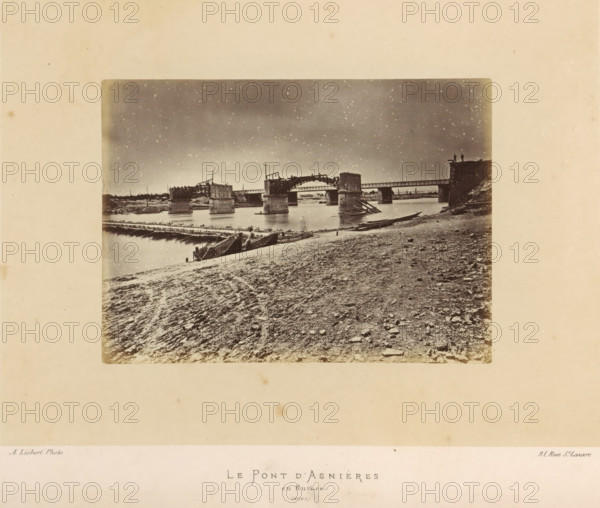 View of the remains of the bridge of Asnières-sur-Seine after the destruction by the Paris Commune, Le Pont d'Asnières and Ruines, photograph, page, number: '(No. 67)', address: '31, Rue St. Lazare', photographer: Alphonse-Justin Liébert, Asnières-sur-Seine, 1871 - 1872, Alphonse-Justin Liébert, photographer, paper, albumen print, height 99 mm x width 135 mm, ruin of a building, architecture, bridge, Paris Commune (1871), A sepia-toned photograph showing a riverbank foreground with a textured, rocky shore and scattered stones, a few wooden boats drawn up at the water's edge, and a timber walkway or floating bridge extending across the water toward a partially ruined bridge structure with several stone piers and damaged wooden arches; the sky appears mottled and grainy above the bridge, and two small human silhouettes stand on a raised platform or abutment at the far right of the bridge.
